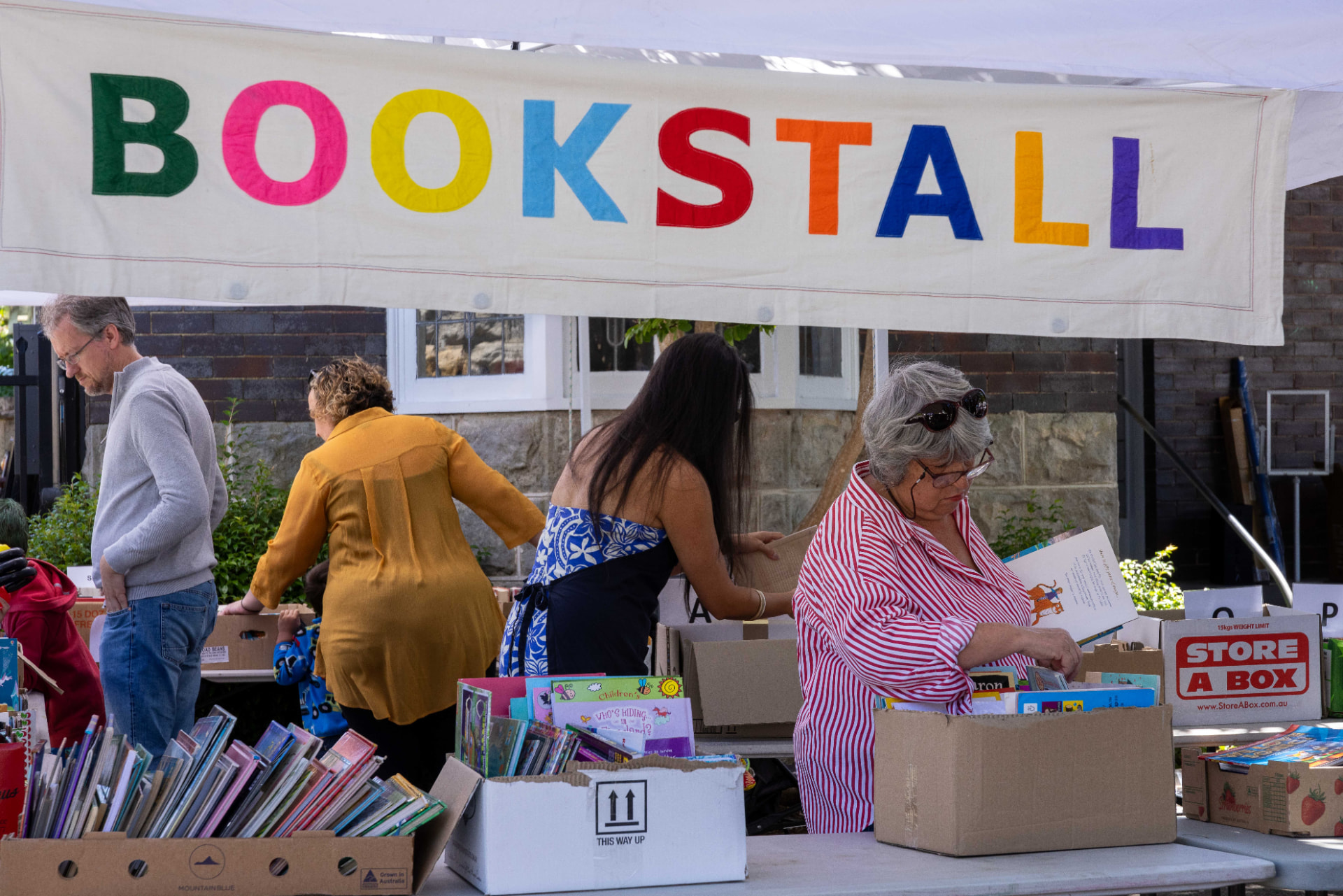 Shoppers browsing boxes of books under the colourful Book Stall banner